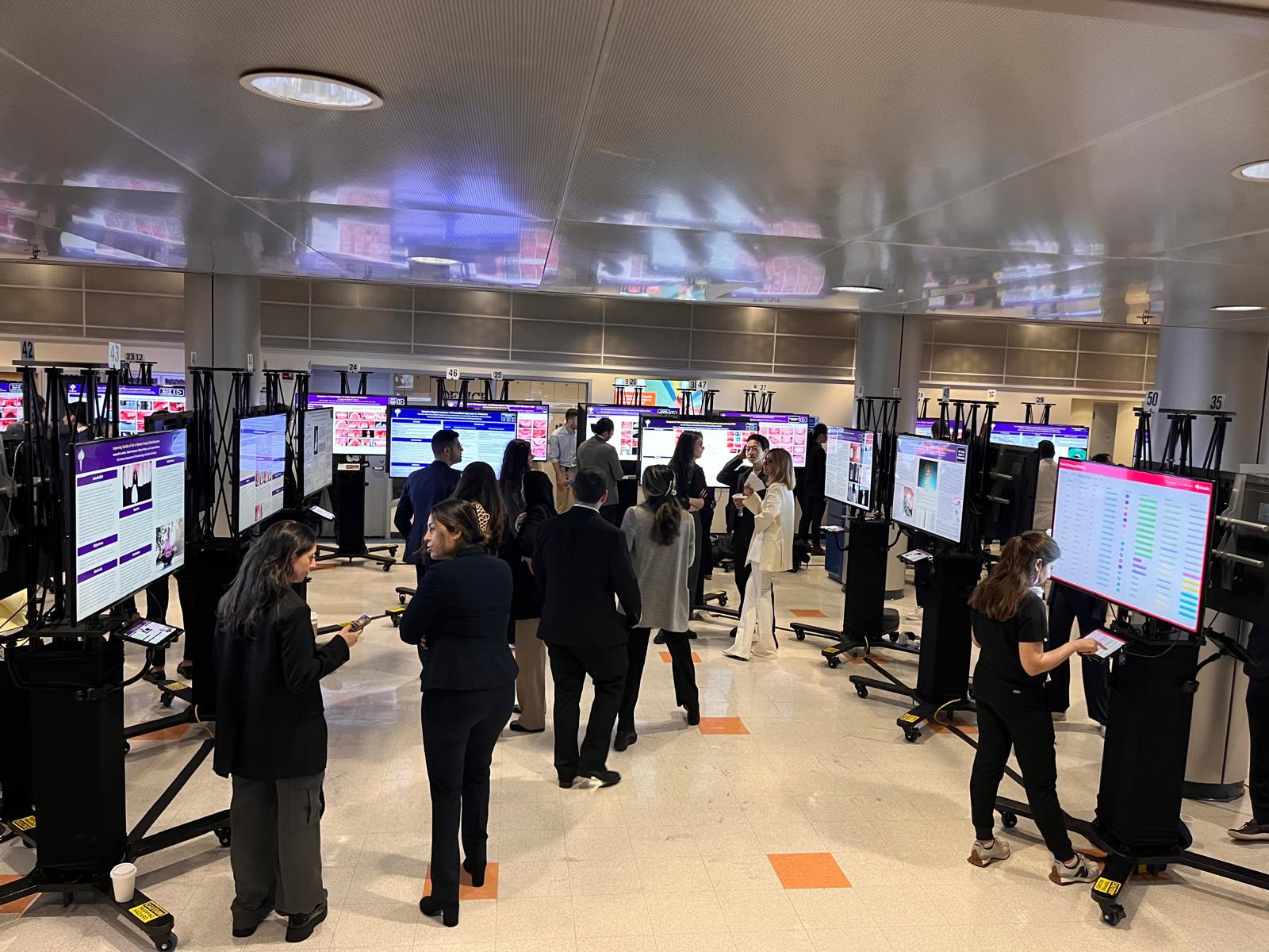 Attendees gathered around digital poster displays in a bright conference space
