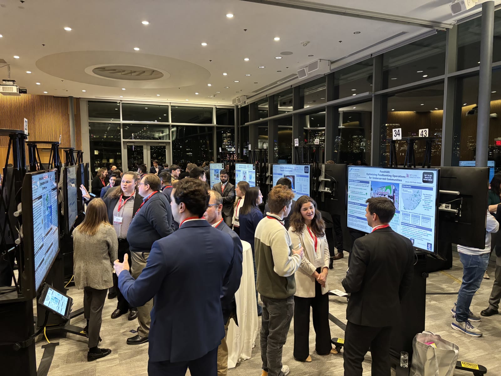 Attendees gathering around digital poster displays at an evening conference